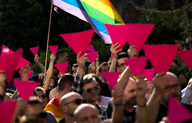 People hold up pink cardboard triangles and wave a rainbow flag during a gathering in support of the LGBT community in Chechnya. Photo: Courtesy U.S. Mission OSCE/Madrid, 2017/AP