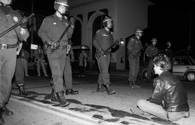 A single activist sits down in the middle of Castro Street as San Francisco police march in riot formation down the street on October 6, 1989. Photo: Rick Gerharter
