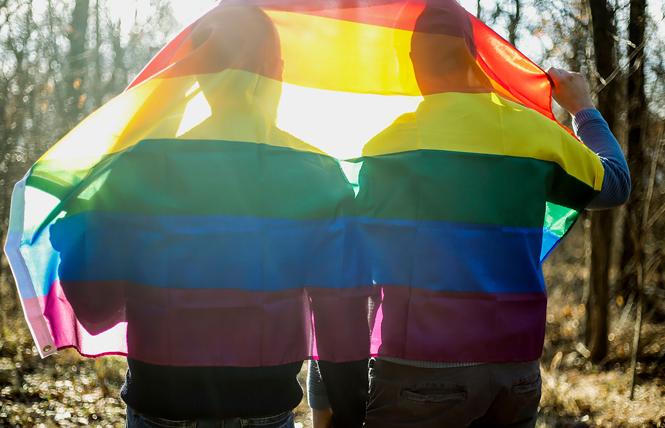 A gay couple walks through the woods draped with a rainbow flag. Photo: Courtesy Human Rights Campaign
