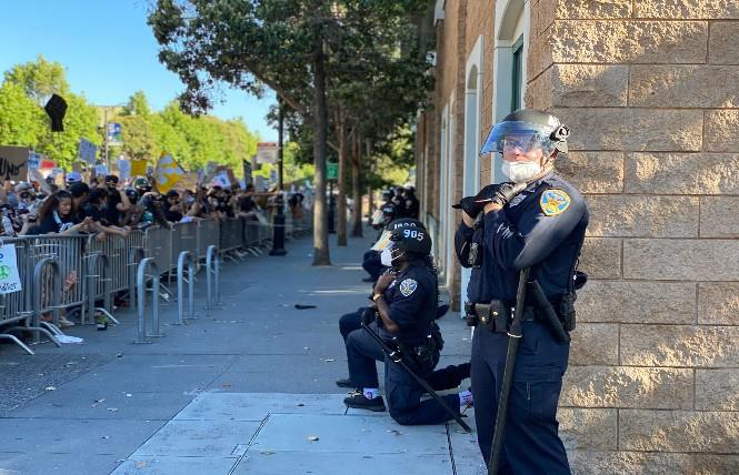 Outside Mission Station, some San Francisco Police officers take a knee, while one does not, during Wednesday's protest against the police killing of George Floyd in Minneapolis. Photo: John Ferrannini
