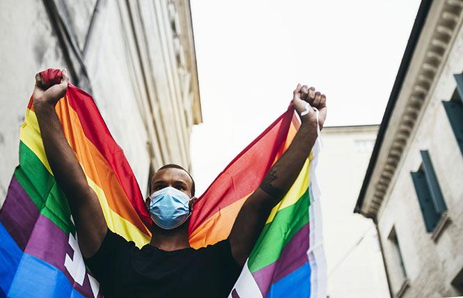A masked demonstrator holds up a rainbow flag. Photo: AdobeStock