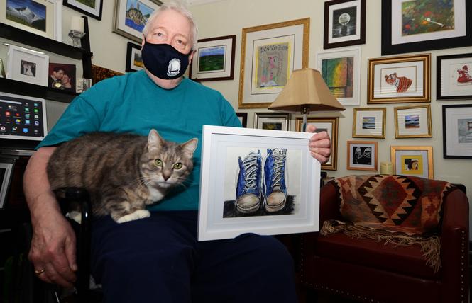 Brian Lynch sits with his cat, Lil Guy, and holds one of his favorite paintings. His other works are on the two walls behind him. Photo: Rick Gerharter