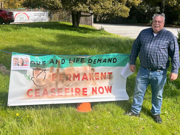The Reverend Jim Mitulski stands next to the damaged ceasefire banner outside of the Congregational Church of the Peninsula. Photo: Courtesy Congregational Church of the Peninsula